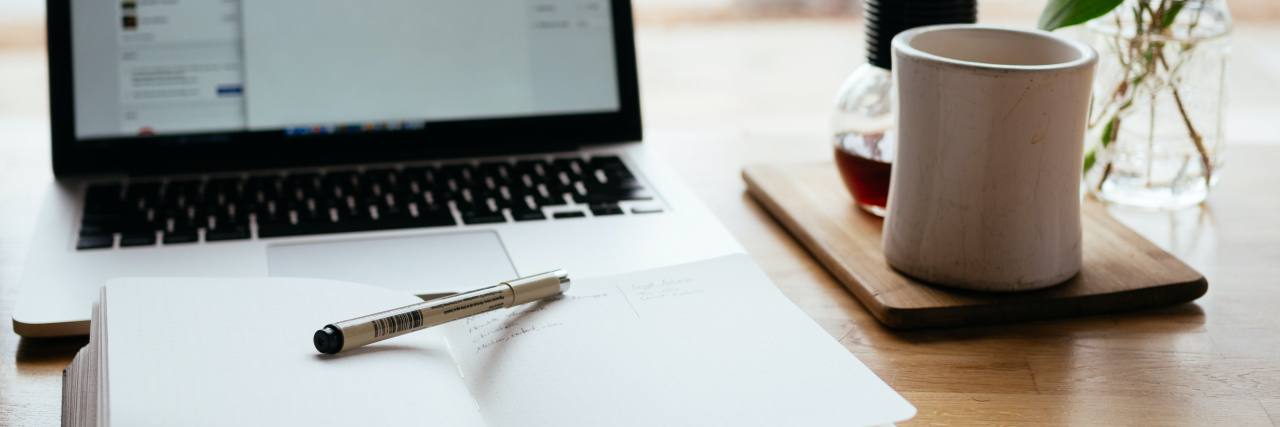 The Mighty's Top 10 Most-Read Stories of 2021 A laptop sitting with an open notebook in front of it. A pen rests on the notebook, and to the right there's a white coffee mug and a little pot of coffee. It's bright and airy.