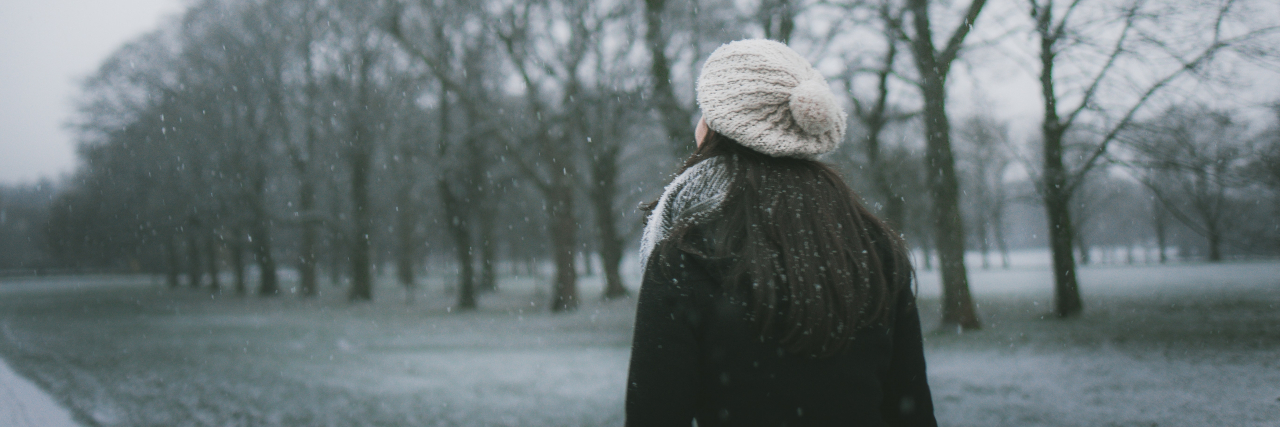 Back of a woman bundled up, walking outside in the snow