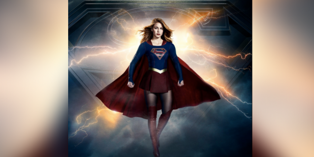 Supergirl wearing red cape in front of stormy sky