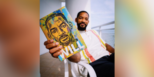 Will Smith holding a copy of his book "Will" sitting on a porch with blue sky in the background