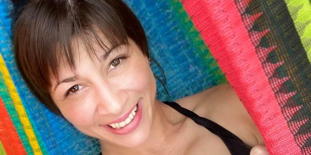 What Helps Alexandria, 38, With Fibromyalgia A woman with brown hair and brown eyes wearing a black tank top with the phrase "Work of Art" written on it in white smiles.