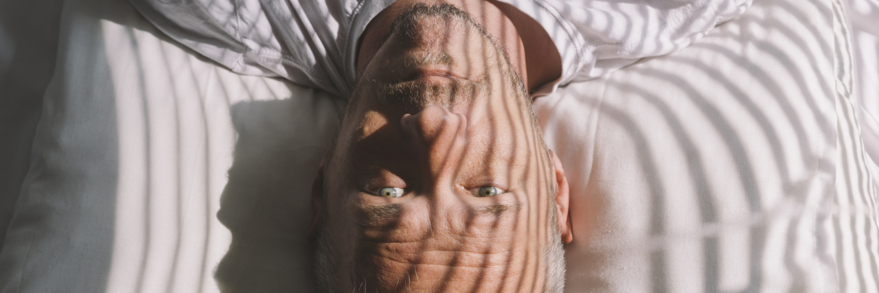 Man lying in bed with eyes open, sun peaking through the window