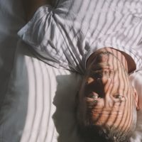 Man lying in bed with eyes open, sun peaking through the window