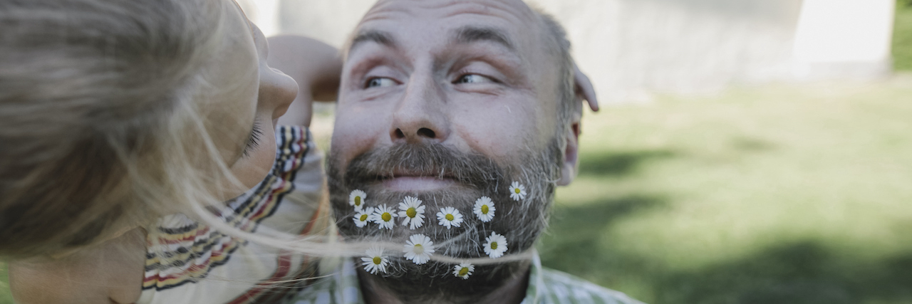 Portrait of smiling man with daisies in his beard playing with little daughter in the garden