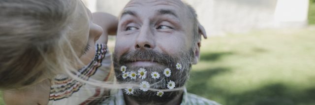Portrait of smiling man with daisies in his beard playing with little daughter in the garden