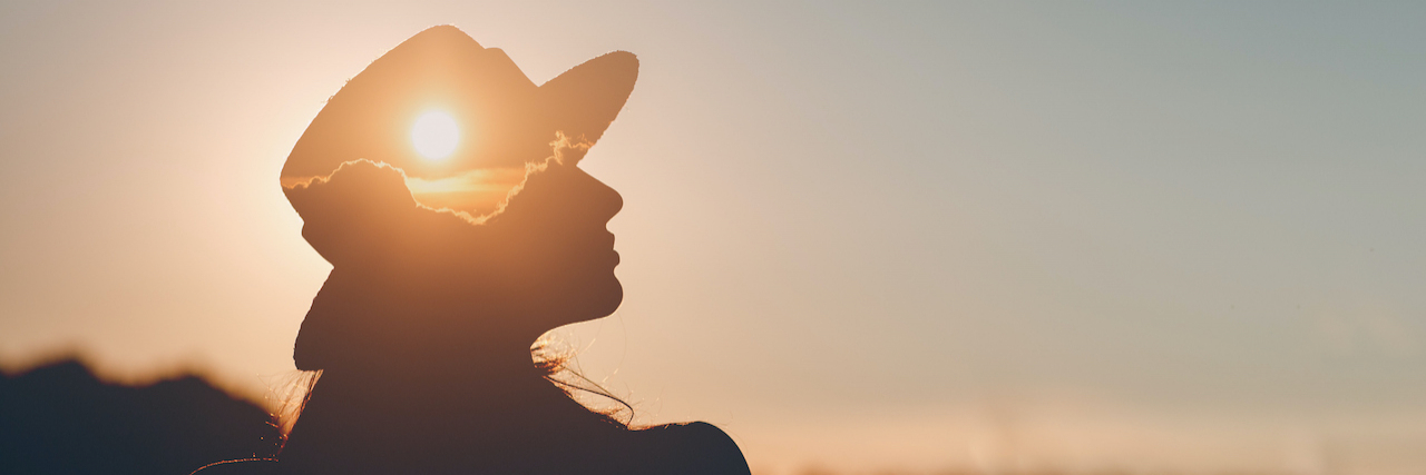 Silhouette of person wearing a hat with sunset layered onto it