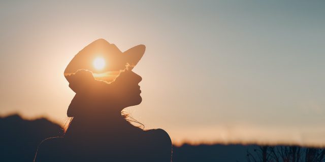 Silhouette of person wearing a hat with sunset layered onto it