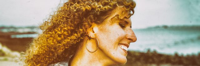 Smiling curly hair woman with large headphones walking outdoors.