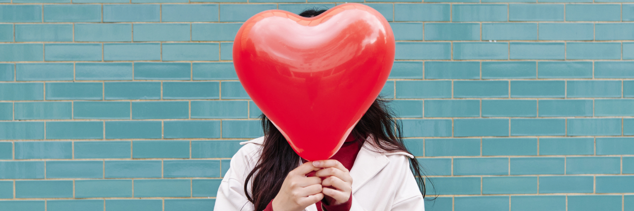 Woman covering face with red heart shape balloon