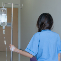 the back view of a younger woman in a hospital walking with an IV machine