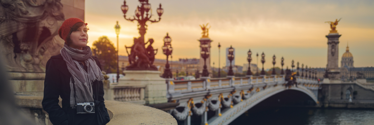 How Moving to a New Country Made Me Confront My Sexual Abuse Woman with a camera around her neck standing on Pont de la Concorde in Paris in morning.