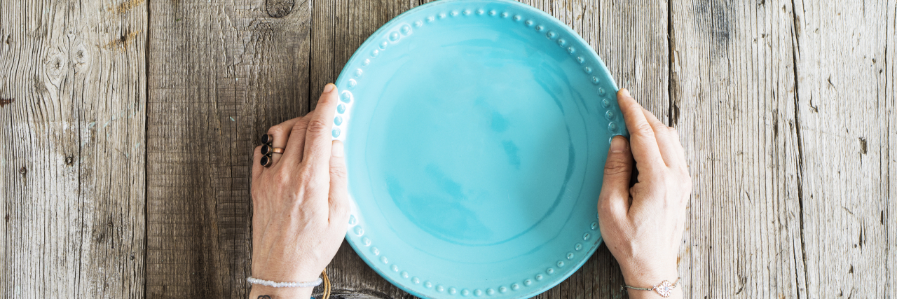 Questions Not to Ask Someone With a Gastroparesis Feeding Tube Woman hands holding blank plate on wooden table.