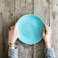 Woman hands holding blank plate on wooden table.