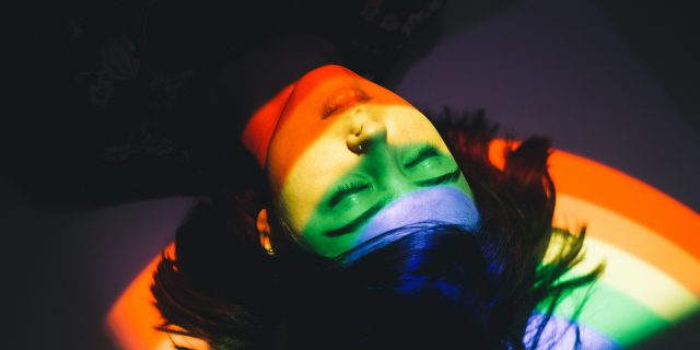 How My OCD Relates to My LGBTQIA+ Identity  Woman laying with eyes closed and light from rainbow over her face