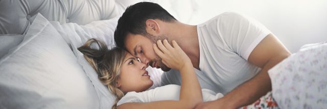 Man and wife holding each other in bed, looking passionately at one another