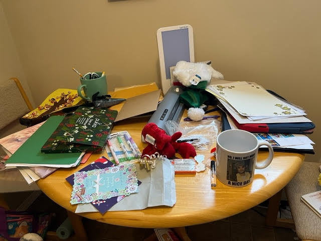 A table with clutter on it. There's assorted letters and scrapbooking tools, two months, and old mail.