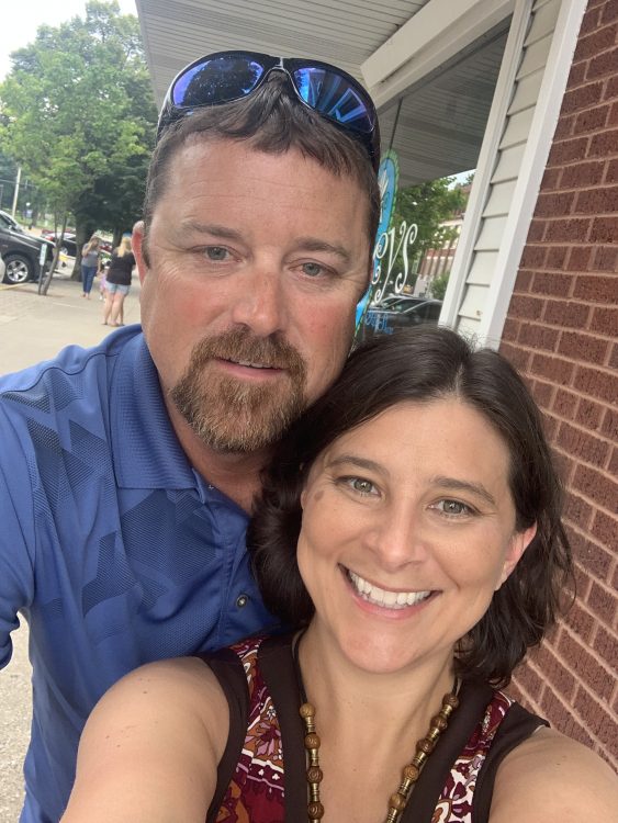 A white woman with brown hair stands beside her partner, a white man.