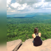 Photo of author; back of a young woman sitting on a rock overlooking mountains and trees