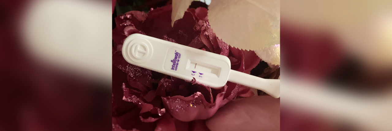 How COVID-19 Forced Me to Finally Battle My Hyper-Independence A negative COVID-19 self test. It's white with a single purple line in front of a backdrop of purple flowers