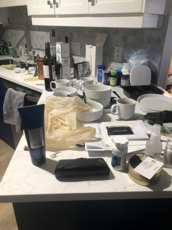 A kitchen counter with a lot of toiletries, dirty dishes, and clutter all over it.