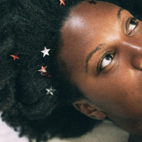close up photo of a woman lying on a white cloth surfce with small stars in her hair