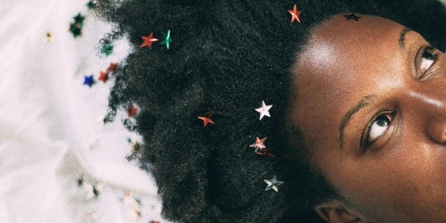 close up photo of a Black woman lying on a white cloth surface with small stars in her hair
