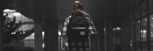 photo of a young boy walking alone through hallway at school alone with a backpack and his head down