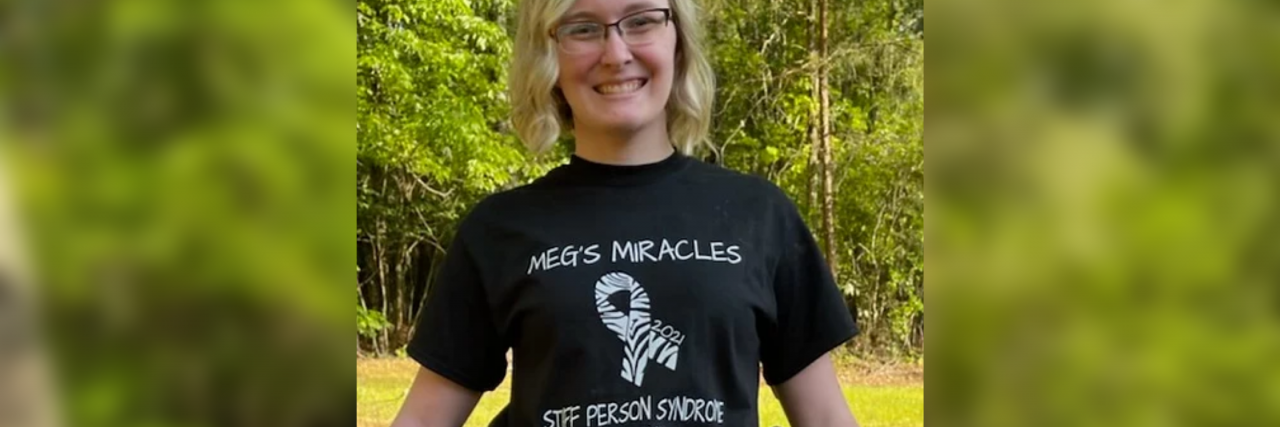 What It's Like Having a Feeding Tube Due to Stiff Person Syndrome Meg wearing a stiff person awareness t-shirt and sitting in her wheelchair.