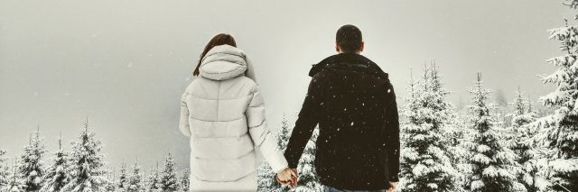 Back of a man and woman in winter jackets holding hands