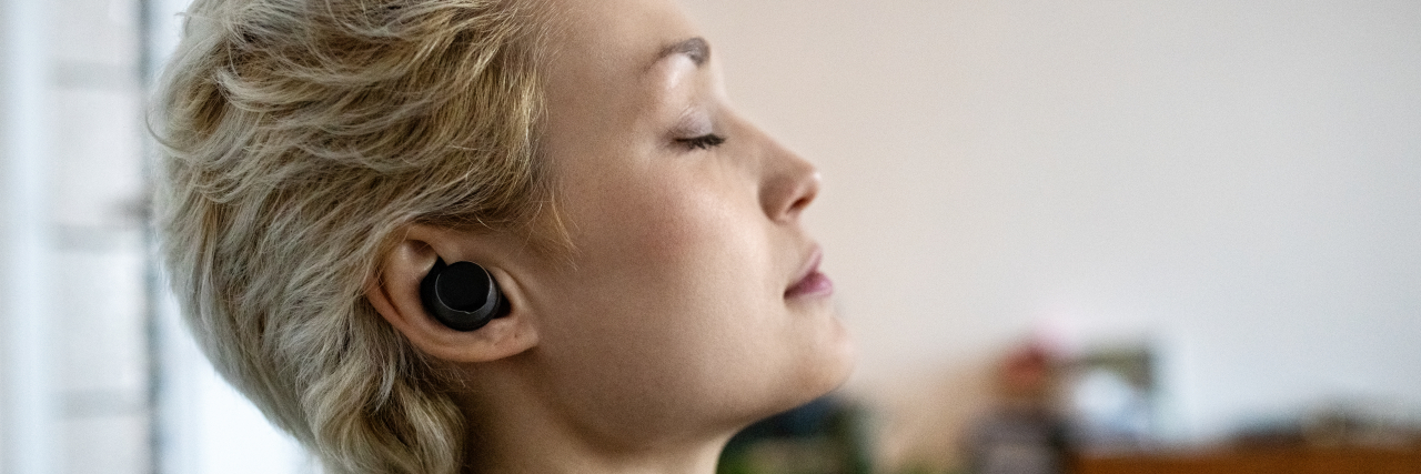 Learning to Breathe Deeply With Trauma and PTSD A person with blonde hair wearing a teal sweater listens on ear speakers with their eyes closed.