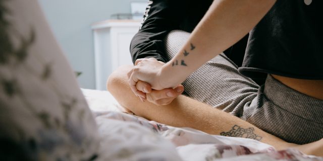 intimate photo of two people sitting on a bed with legs crossed and holding hands