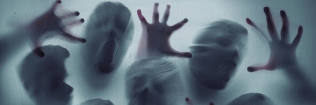 Abstract ghost faces and hands pressed up against a screen
