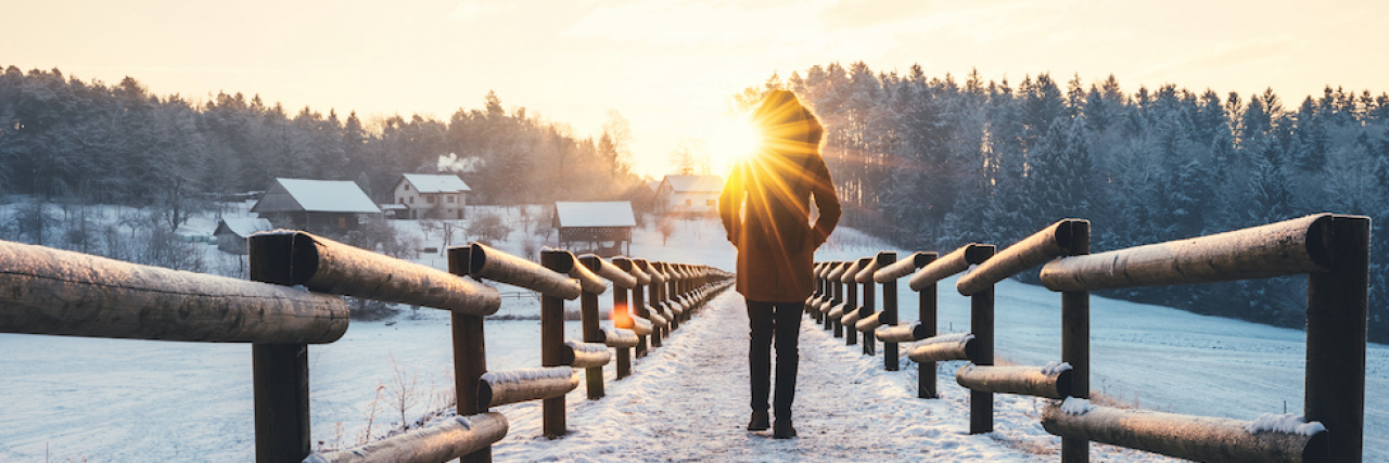 Woman walking at the frozen lake. Morning sun is peaking out from the trees.