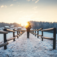 Woman walking at the frozen lake. Morning sun is peaking out from the trees.