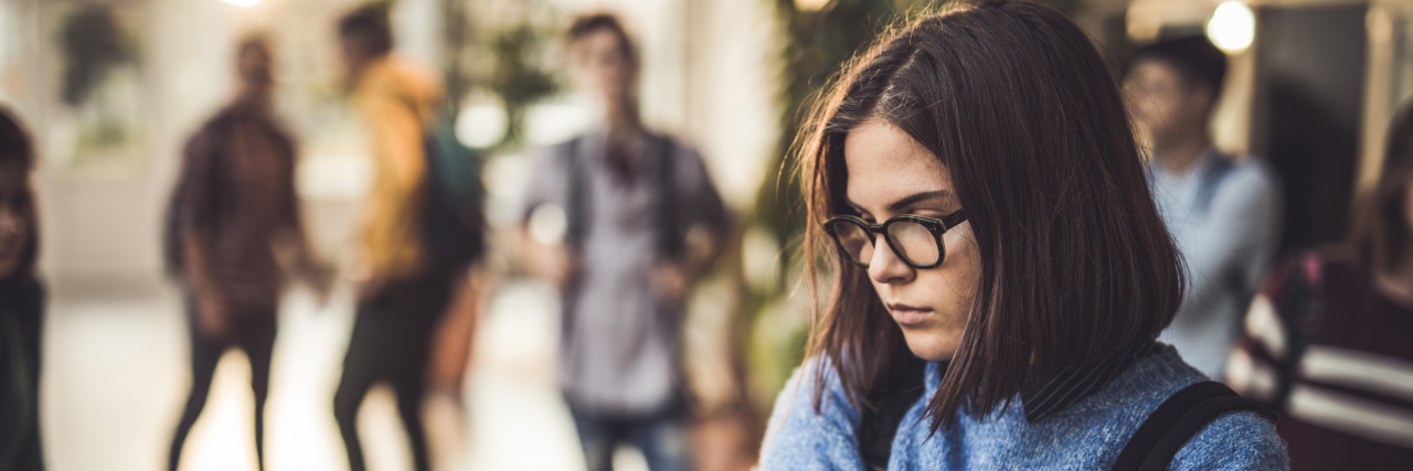 How Social Anxiety Has Impacted Me Throughout My Life Female student with glasses looking down shyly with classmates standing behind her