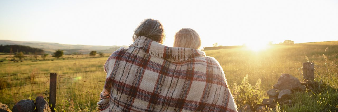 What I Want My Future Partners to Know About Loving Me With Bipolar Disorder A couple sitting on a field with a blanket wrapped around them, sun shining