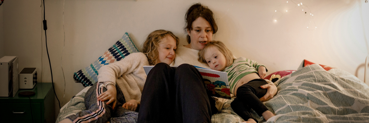 Mother reading picture book while sitting with children in bedroom.
