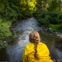 Woman in a yellow jacket is sitting on a bridge over the river.