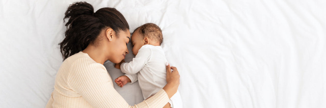 Black mother hugging baby on bed