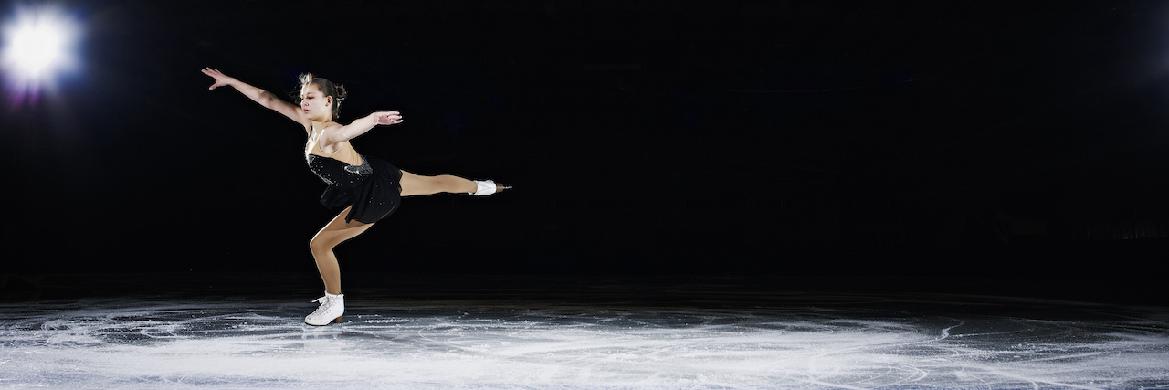 Female figure skater landing a jump during a performance on ice rink in arena