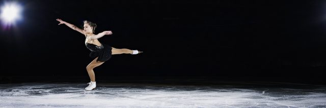 Female figure skater landing a jump during a performance on ice rink in arena