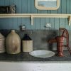 Antique kitchen counter with old jugs, water pump, sink, mirror and shelf above the counter