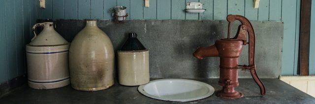 Antique kitchen counter with old jugs, water pump, sink, mirror and shelf above the counter