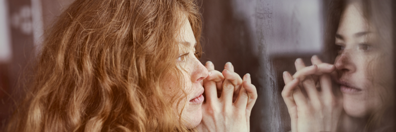 What the F in FOMO Stands for When You Have Debilitating Chronic Illness Woman looking out of window at her reflection.