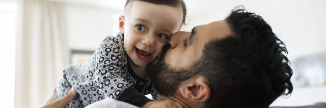 Loving father kissing baby girl while sitting on sofa at home.