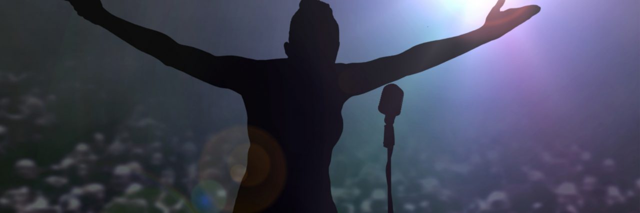 11 Jokes That One Woman Tells When She's Suicidal A women on stage silhouetted in a spotlight spreads her arms and bows to the large crowd.