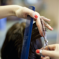 Hands holding comb, scissors and hair by a person's head during haircut