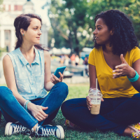 A white woman and Black woman in the park drinking coffee and talking