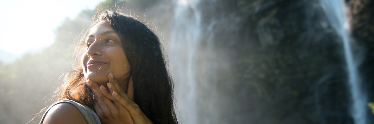 Woman of color standing in front of waterfall and looking to the side