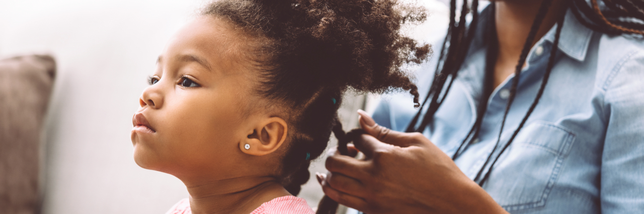 Little girl getting her hair twisted by her mom.